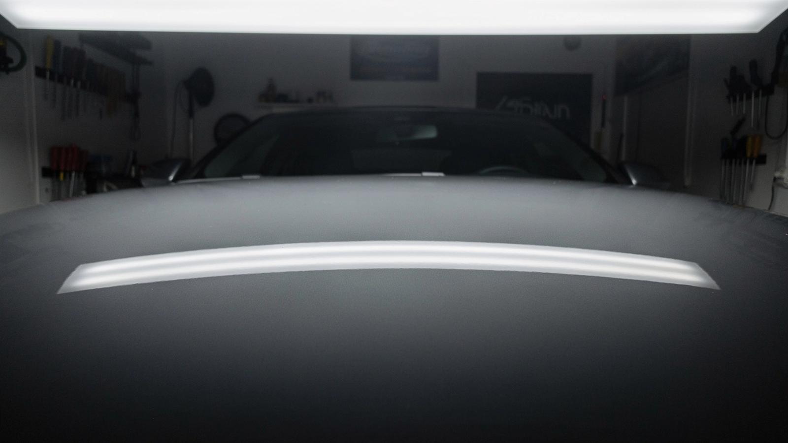 Dark car hood under LED inspection light after machine paint correction and ceramic coating